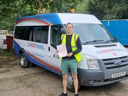 Man standing beside a minibus with "GS Driver Training" branding, showcasing D1 driving training in Wiltshire.